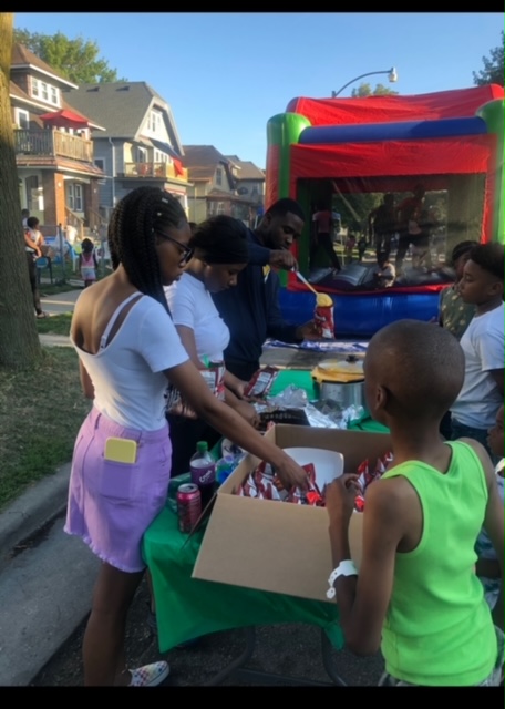 Neighbors serving food at a block party with a bounce house